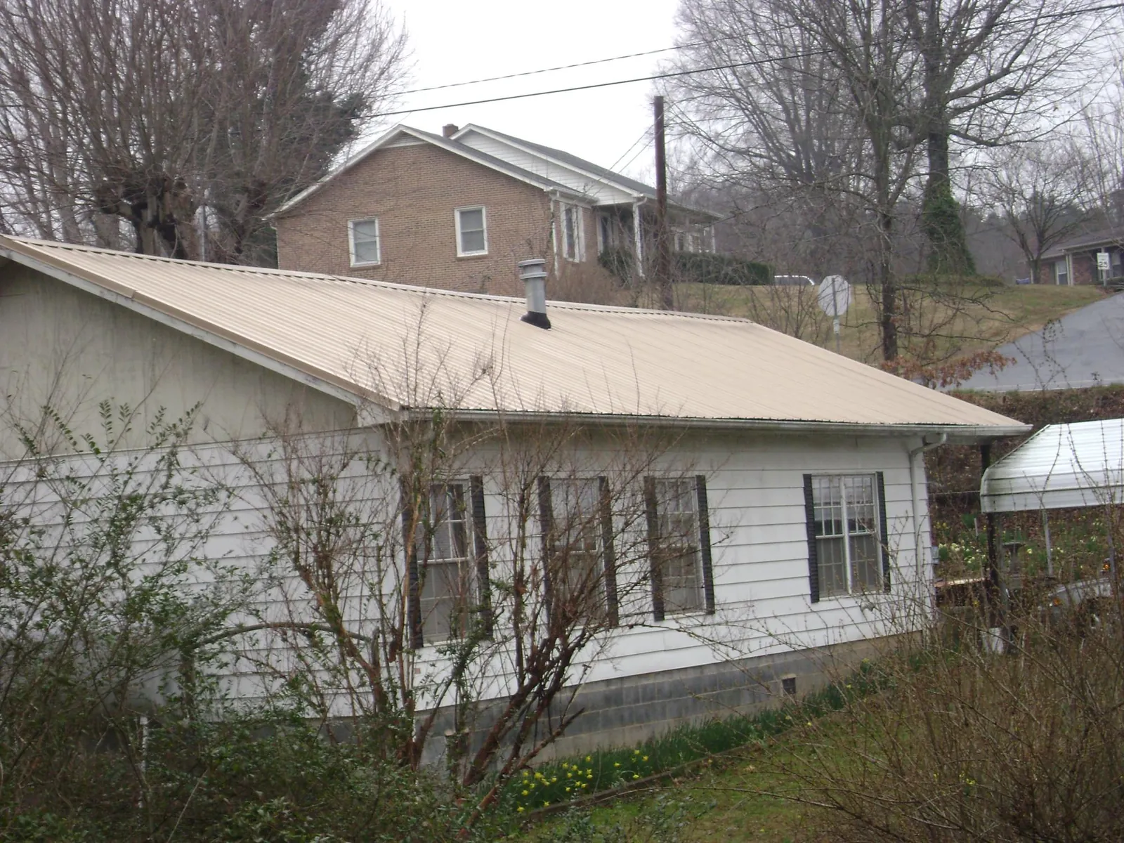Tan metal roof on a white sided house set into a hillside — Commercial Roofing by Roofing Brothers in Elmhurst